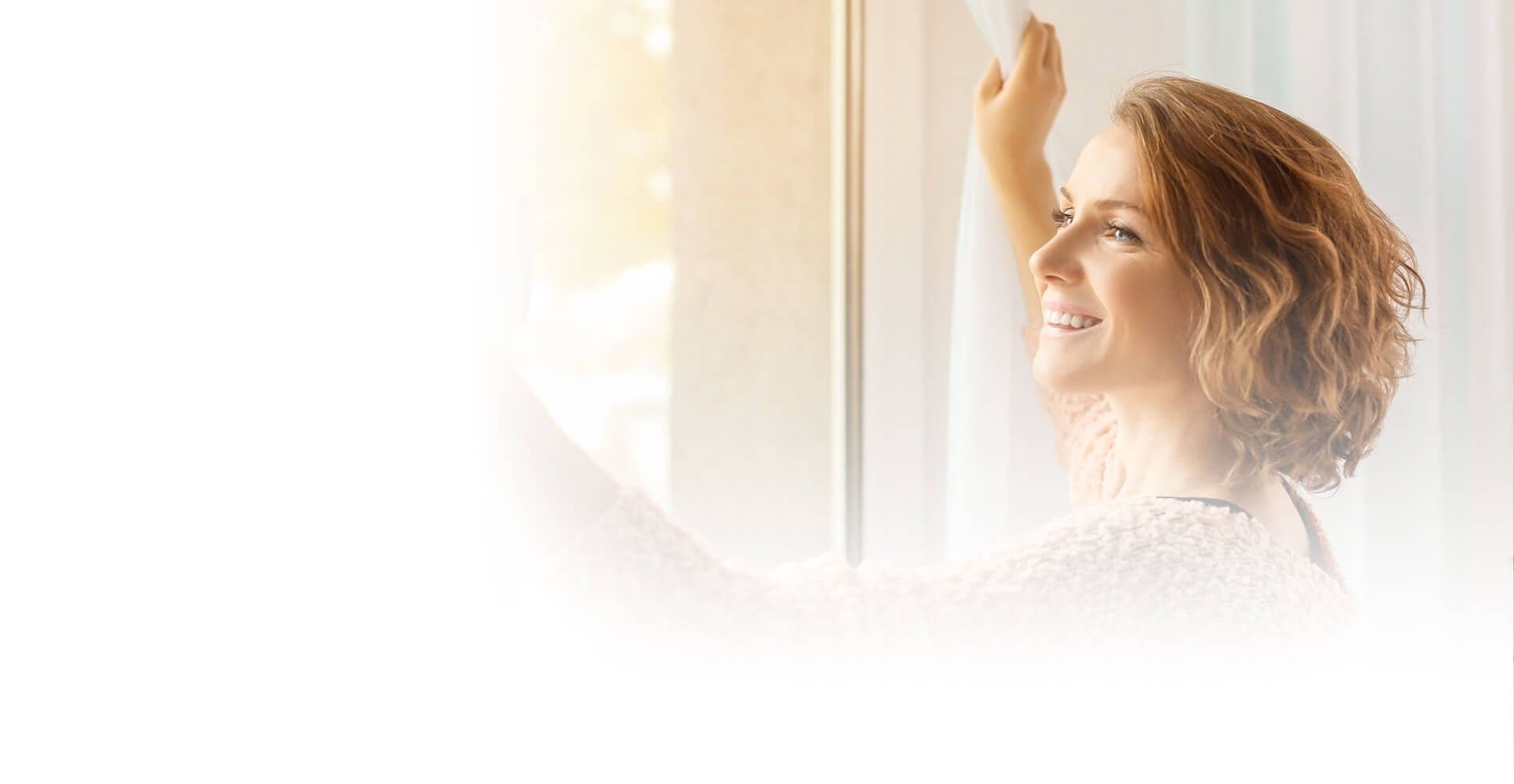 A person smiles as they open curtains.