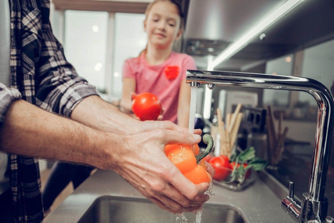 A person washes produce in a kitchen sink.