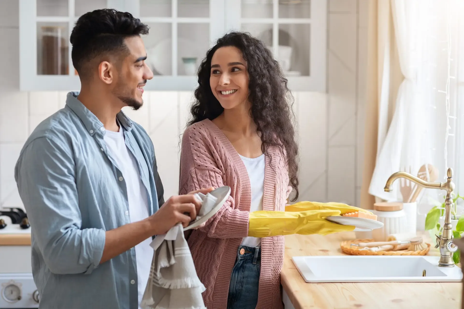 A couple smiles at each other while washing dishes together.