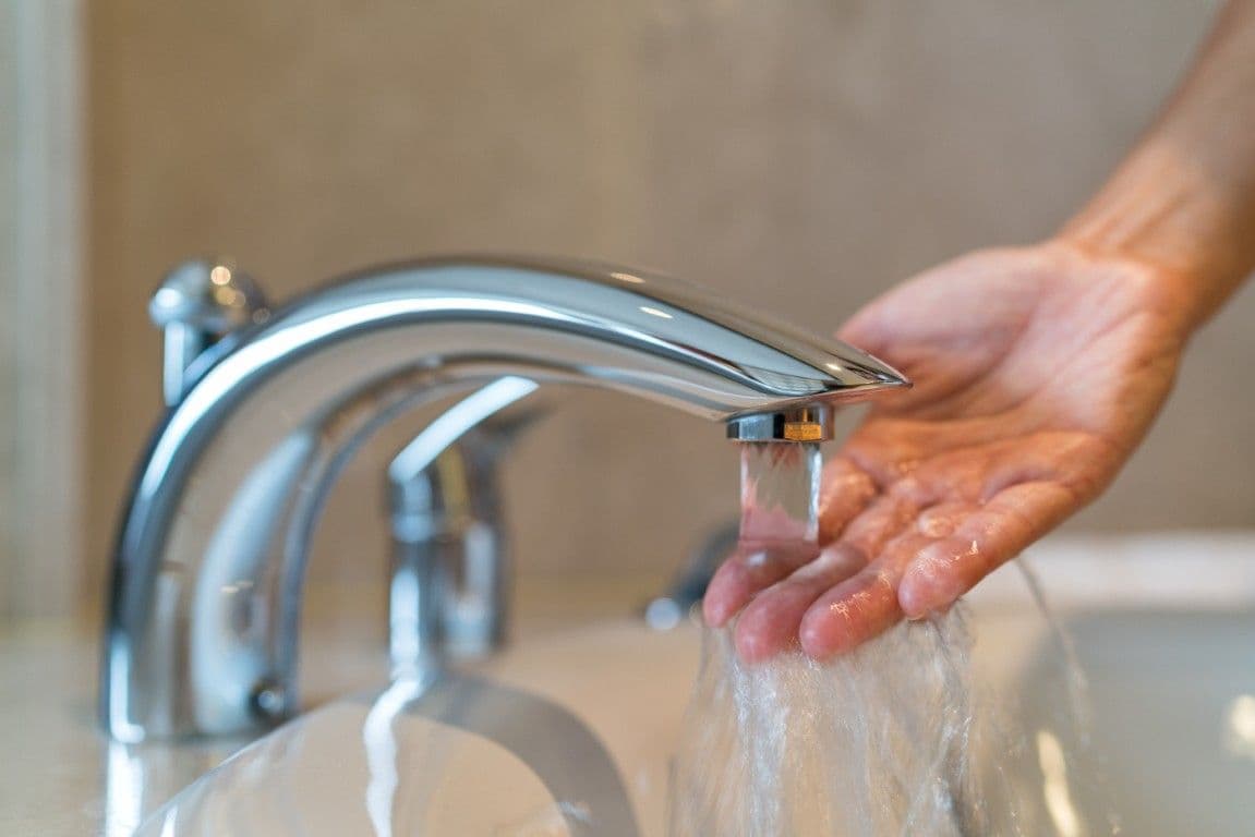 A person holds their hand under a running faucet.