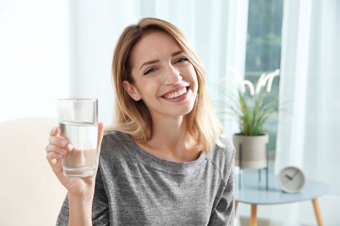A person is smiling and holding a glass of water.