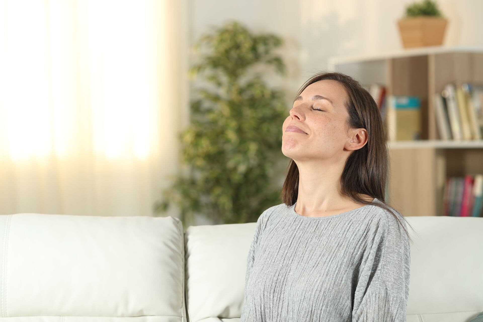 A person leans back on a couch with their eyes closed and breathes deeply.